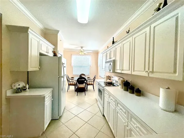 Kitchen featuring white appliances, ornamental molding, light countertops, a textured ceiling, and white cabinetry