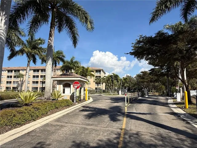 View of asphalt road with traffic signs, a gated entry, and curbs