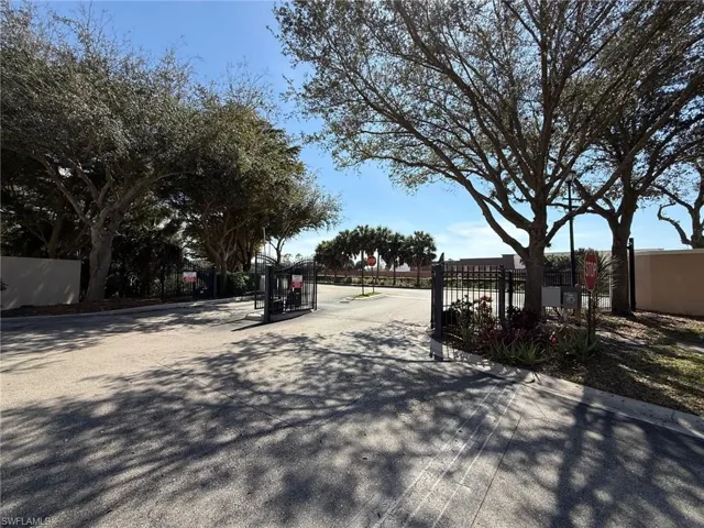 View of asphalt street featuring a gated entry, a gate, and curbs