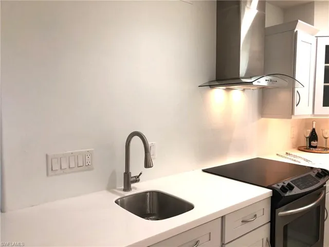 Kitchen with wall chimney range hood, electric range, a sink, light countertops, and white cabinetry