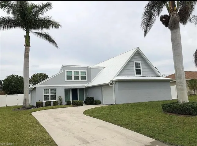 View of front facade featuring driveway, stucco siding, fence, and a front lawn