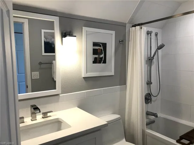 Bathroom featuring tile walls, toilet, shower / bathtub combination with curtain, vanity, and lofted ceiling