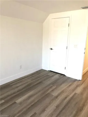 Unfurnished bedroom featuring baseboards, lofted ceiling, and dark wood-style flooring