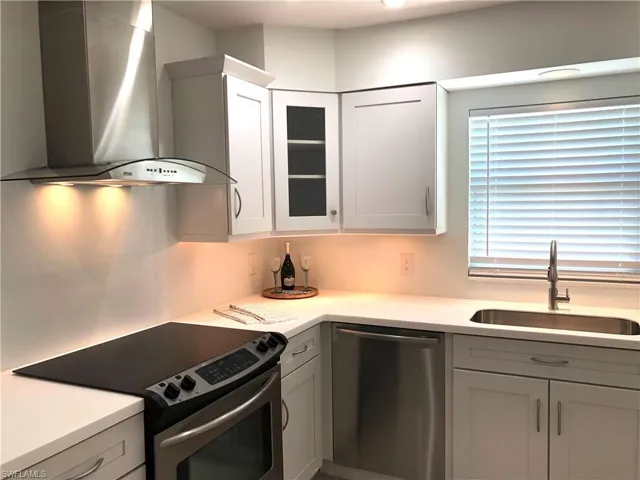 Kitchen with wall chimney exhaust hood, appliances with stainless steel finishes, a sink, light countertops, and glass insert cabinets