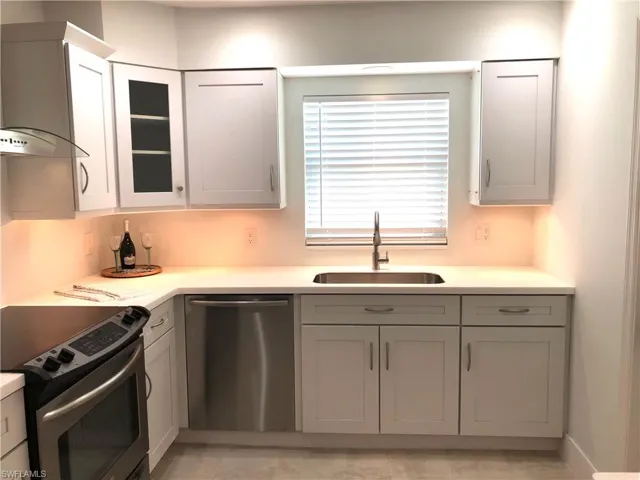 Kitchen featuring stainless steel appliances, a sink, wall chimney exhaust hood, light countertops, and glass insert cabinets