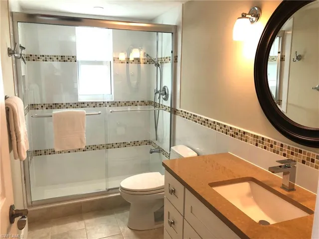 Full bath featuring a shower stall, toilet, tile walls, vanity, and tile patterned floors
