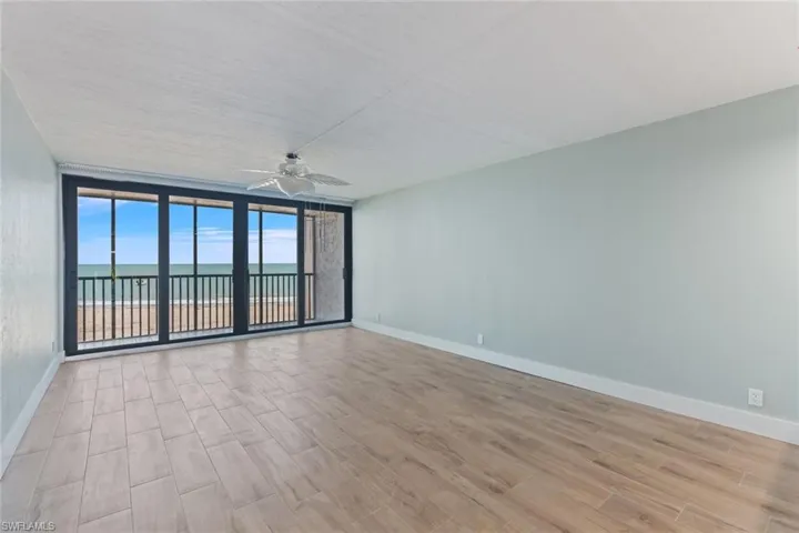 Unfurnished room featuring baseboards, a water view, ceiling fan, a wall of windows, and wood finished floors