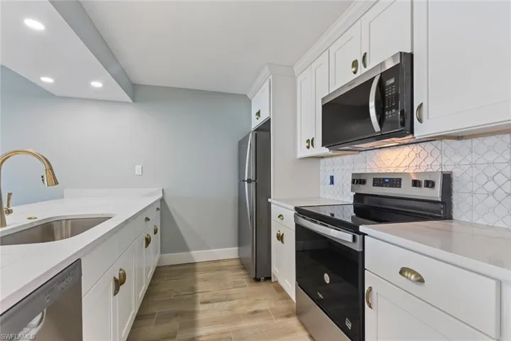 Kitchen with appliances with stainless steel finishes, baseboards, recessed lighting, decorative backsplash, and a sink