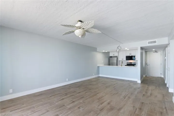 Unfurnished living room with light wood-type flooring, ceiling fan, visible vents, and a textured ceiling