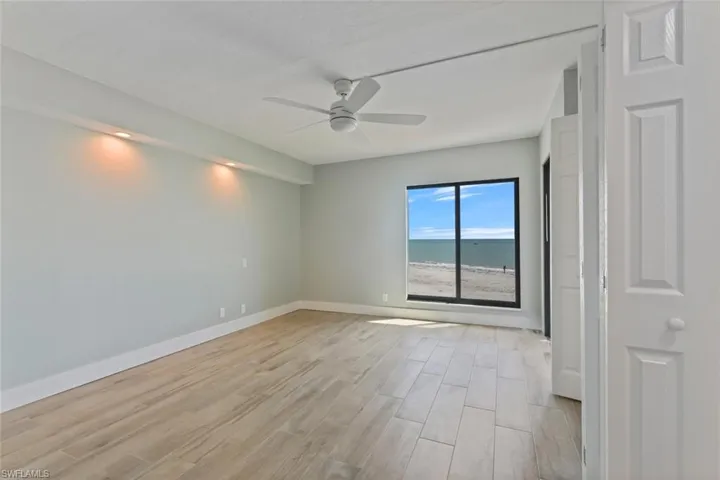 Empty room featuring a water view, light wood-style flooring, a ceiling fan, and baseboards