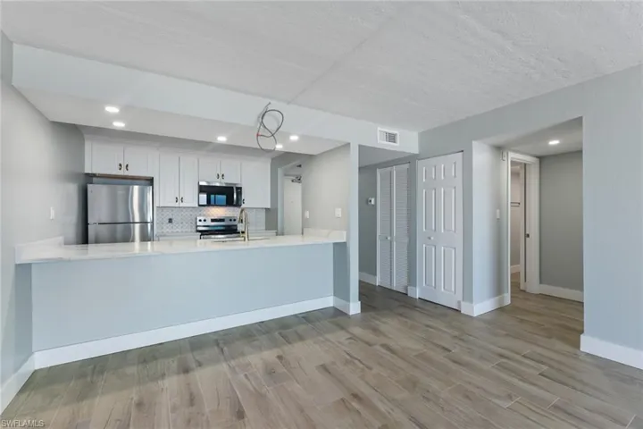 Kitchen with a peninsula, wood finished floors, light countertops, stainless steel appliances, and baseboards