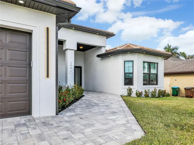 View of exterior entry with stucco siding, a garage, a lawn, and decorative driveway