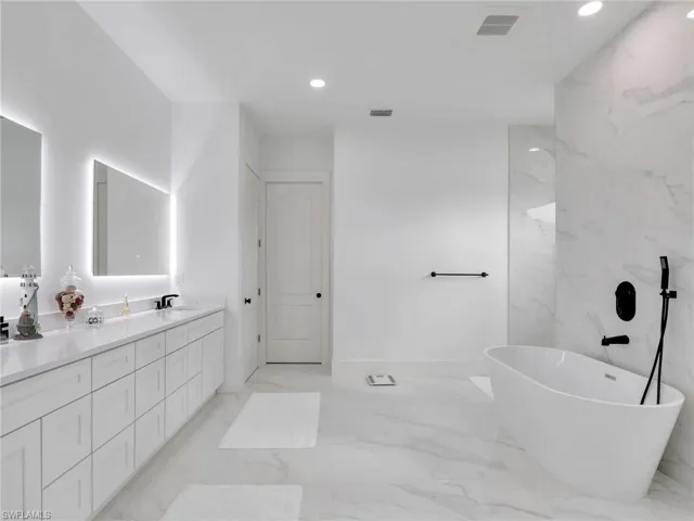 Full bathroom featuring marble tiled floors, double vanity, a freestanding tub, and recessed lighting