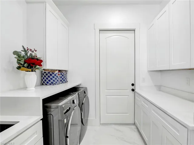 Laundry area with light marble finish floors, washer and dryer, and cabinet space