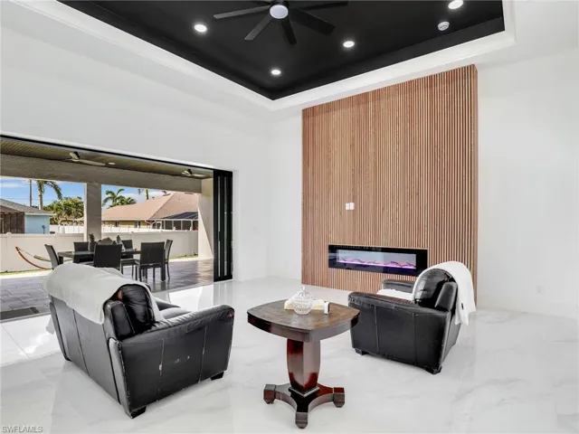 Living area featuring a tray ceiling, a glass covered fireplace, recessed lighting, and marble finish floors