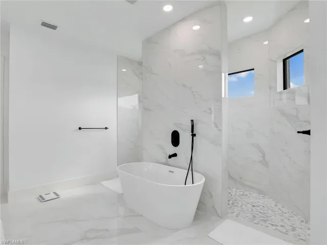 Bathroom with marble tiled floors, a freestanding tub, a marble finish shower, and recessed lighting