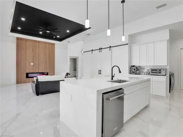 Kitchen with light marble finish flooring, dishwasher, white cabinetry, a kitchen island with sink, and hanging light fixtures