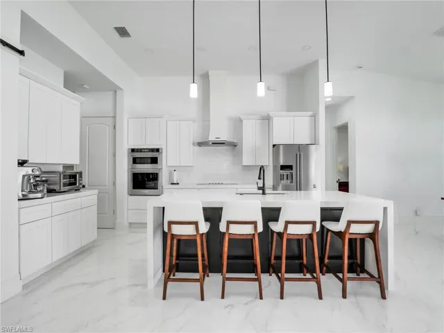 Kitchen with a kitchen breakfast bar, stainless steel appliances, white cabinets, and exhaust hood
