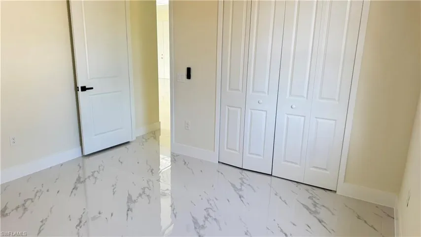 Unfurnished bedroom featuring marble finish floor, a closet, and baseboards