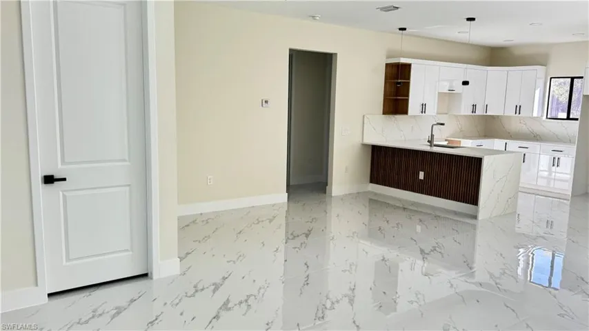 Kitchen with baseboards, marble finish floor, white cabinetry, and a sink