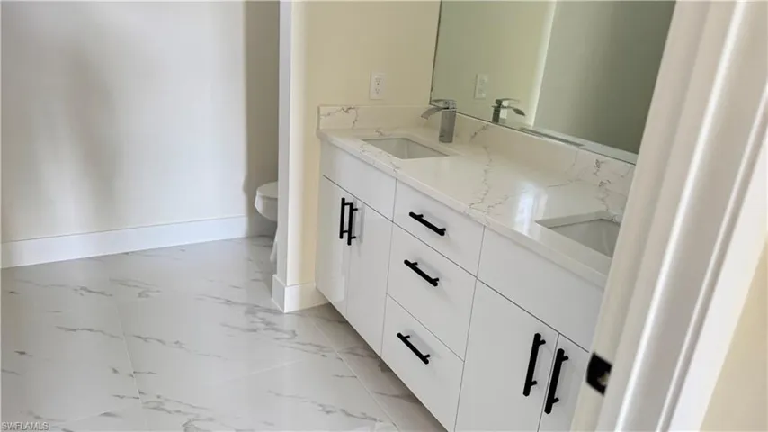 Full bath featuring toilet, a sink, marble finish floor, baseboards, and double vanity