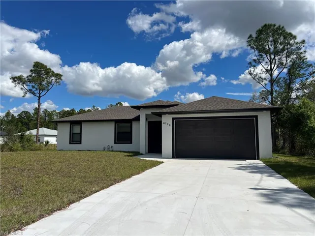 Prairie-style home featuring an attached garage, a front lawn, concrete driveway, and stucco siding