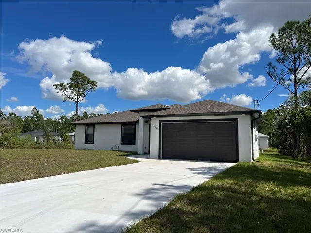 View of front of home with a garage, a front yard, concrete driveway, and stucco siding