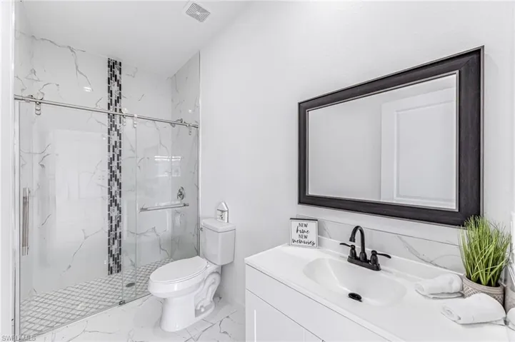 Bathroom featuring a marble finish shower, visible vents, toilet, marble finish floor, and vanity