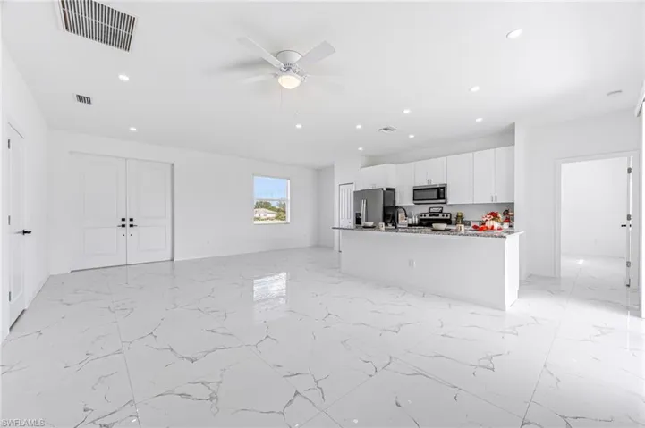 Kitchen with a center island with sink, stainless steel appliances, visible vents, open floor plan, and white cabinets