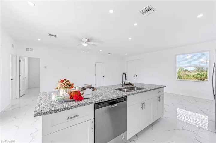 Kitchen with a sink, a center island with sink, white cabinetry, and stainless steel dishwasher