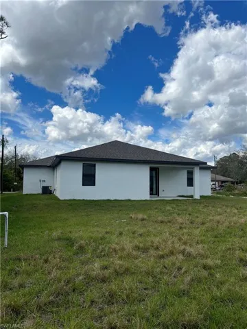 Rear view of property with stucco siding, a yard, and central AC unit