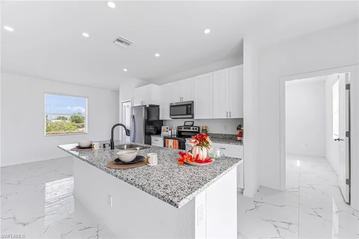 Kitchen with marble finish floor, stainless steel appliances, a kitchen island with sink, and white cabinets