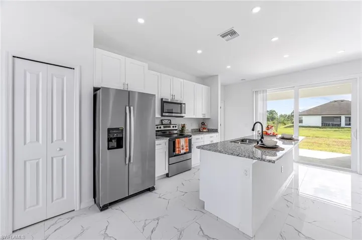 Kitchen with white cabinets, an island with sink, marble finish floor, stainless steel appliances, and a sink
