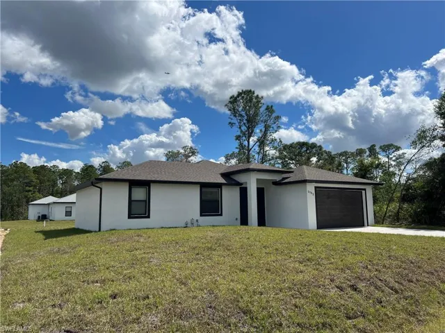 View of front of property featuring a garage, driveway, a front lawn, and stucco siding
