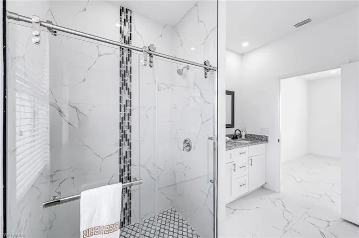 Bathroom with a marble finish shower, visible vents, marble finish floor, vanity, and recessed lighting