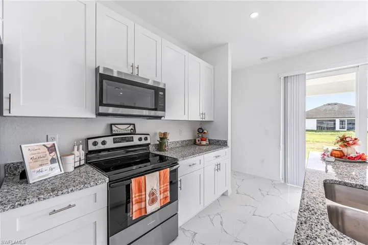 Kitchen featuring appliances with stainless steel finishes, marble finish floor, white cabinetry, and light stone counters