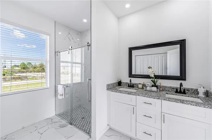 Full bath featuring double vanity, marble finish floor, a marble finish shower, and a sink
