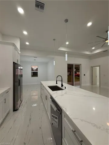 Kitchen featuring light stone countertops, white cabinetry, decorative light fixtures, and recessed lighting