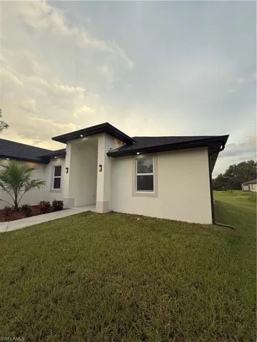 View of front of home with stucco siding, a front yard, and a shingled roof