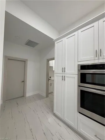 Kitchen featuring double wall oven, white cabinetry, and light marble finish floors