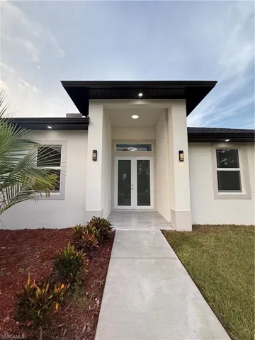 View of exterior entry featuring stucco siding, french doors, and a lawn