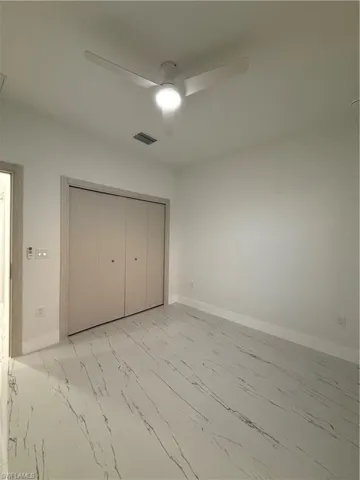 Unfurnished bedroom with light marble finish flooring, a ceiling fan, and a closet