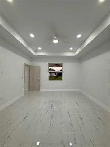 Empty room featuring recessed lighting, a tray ceiling, ceiling fan, and light marble finish floors