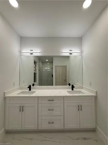 Full bathroom with light marble finish flooring, a shower stall, double vanity, and recessed lighting