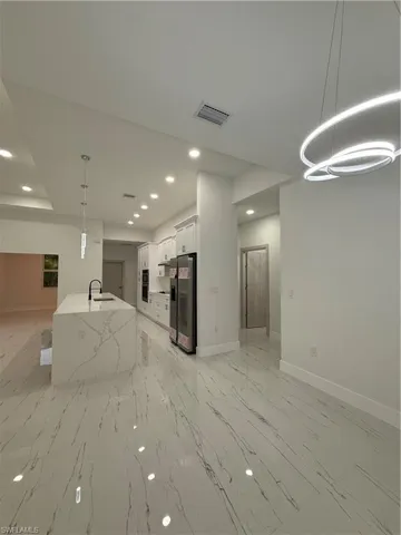 Kitchen with hanging light fixtures, recessed lighting, open floor plan, white cabinetry, and light stone countertops