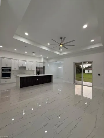 Unfurnished living room featuring a raised ceiling, recessed lighting, light marble finish flooring, and a ceiling fan