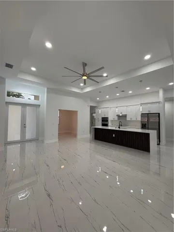 Unfurnished living room featuring recessed lighting, ceiling fan, light marble finish floors, and a tray ceiling