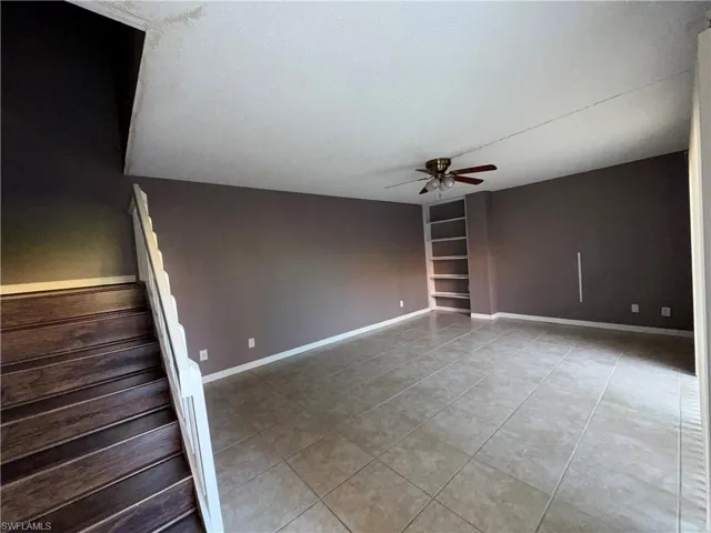Empty room with ceiling fan, light tile patterned floors, built in shelves, and a textured ceiling