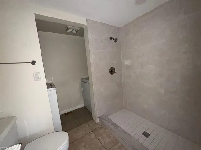 Full bath with a stall shower, light tile patterned flooring, and washer / clothes dryer