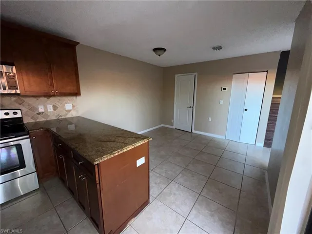 Kitchen featuring stainless steel appliances, a peninsula, light tile patterned flooring, dark stone countertops, and decorative backsplash